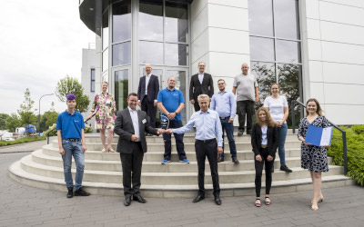 总经理Eugen Dumitrescu在Wedel TRIOPTICS GmbH公司大楼前从IHK副总裁Jan-Henrik Fock(左三)手中接过玻璃奖杯，作为TOP培训公司的奖项。公司的员工和学员也出席了仪式。(图片来源:IHK/Peter Lühr)